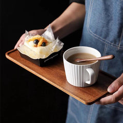 Person carrying rectangular wooden tea tray with coffee mug and pastry