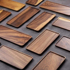 Many rectangular acacia wood serving trays laid out on dark surface, top view