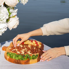 Hands arranging nuts and snacks on pumpkin shaped wooden serving tray