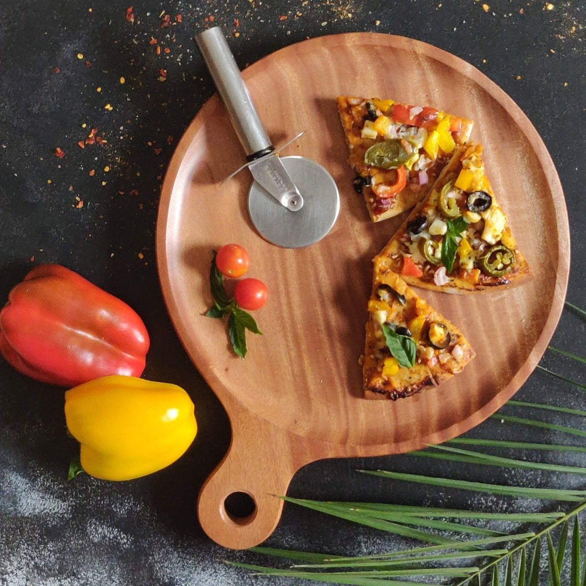 Round wooden pizza platter tray with pizza slices, cutter and peppers