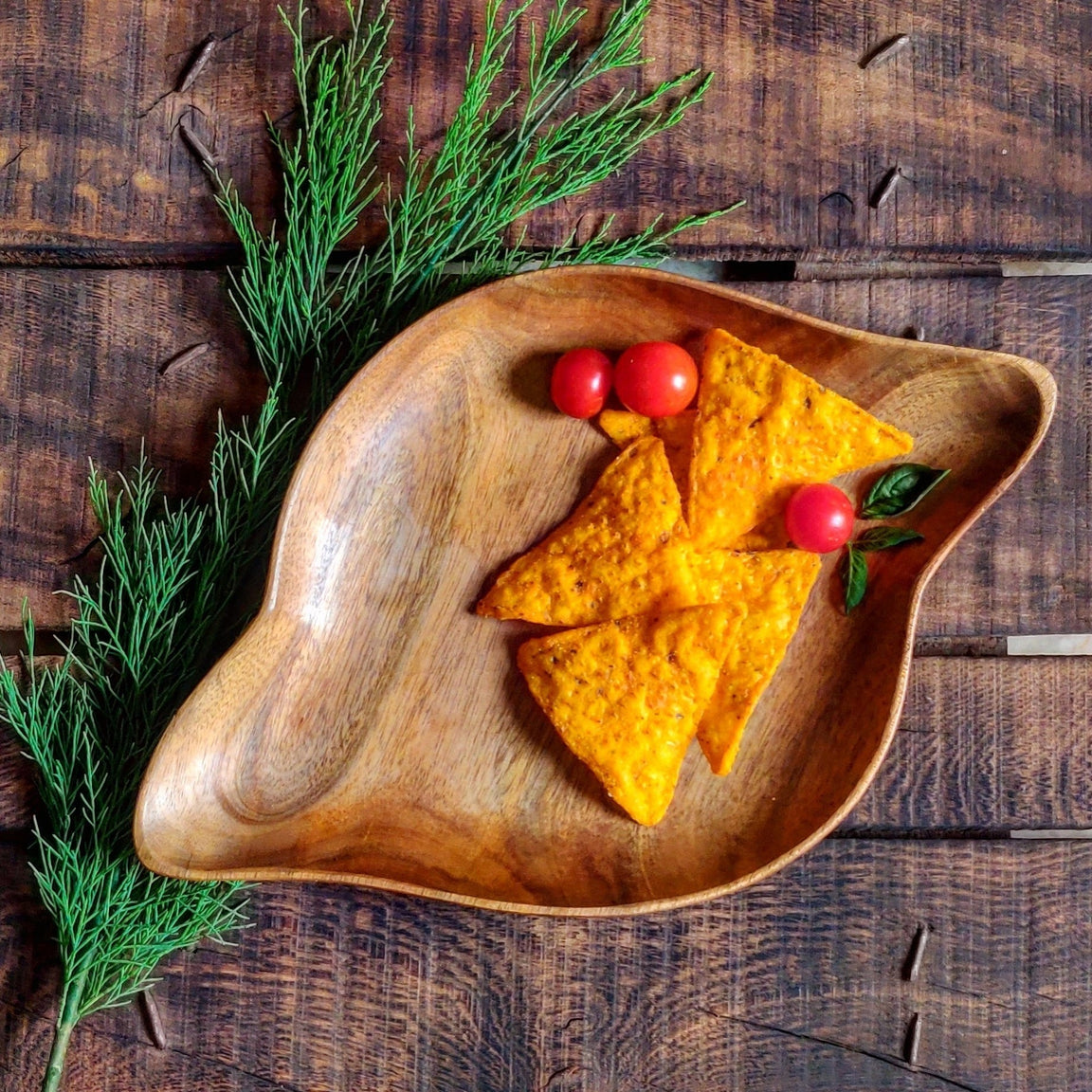 Shell shape wooden platter with nachos and tomatoes on rustic wooden table