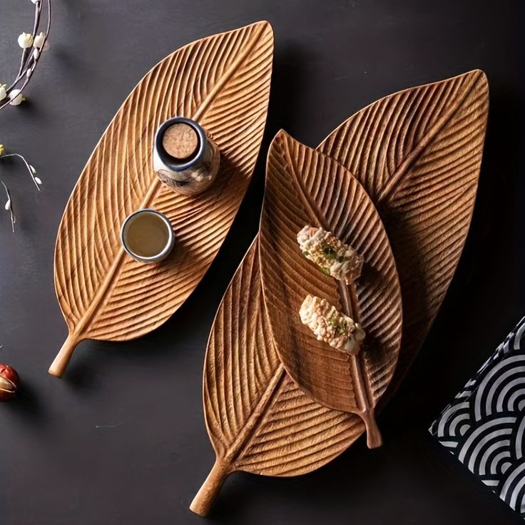 Three carved wooden leaf shaped serving trays holding jewellery on dark surface