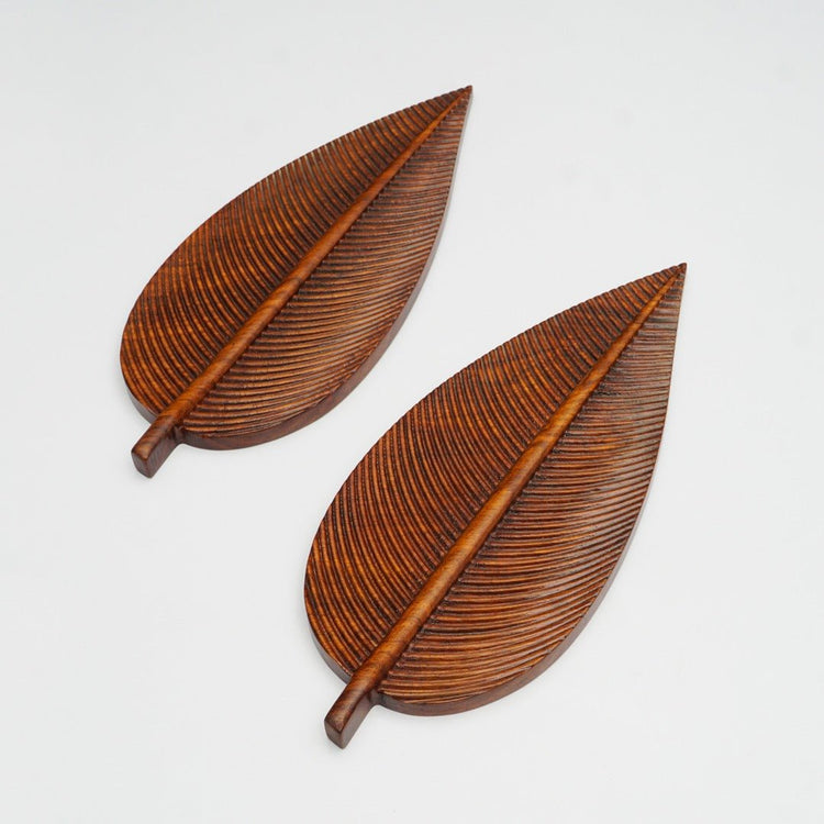 Pair of brown wooden leaf shaped fruit dish trays lying diagonally