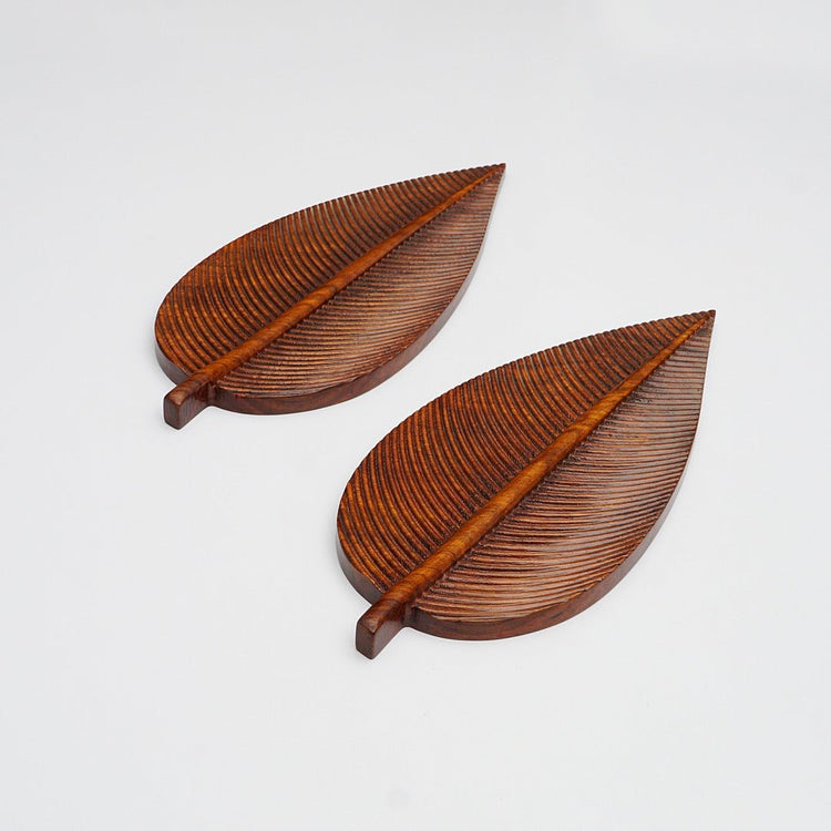 Two brown wooden leaf shaped serving trays with carved veins, angled view