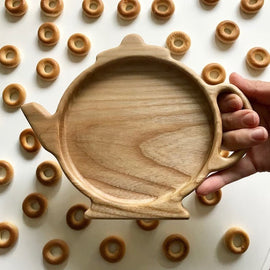 Hand holding teapot shaped wooden serving tray among small ring biscuits
