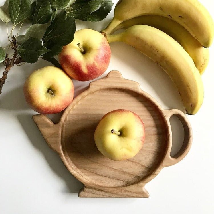 Teapot shaped wooden serving tray with apple beside bananas