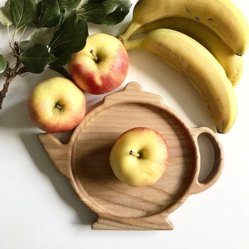 Teapot shaped wooden serving tray with apple beside bananas