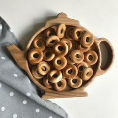 Teapot shaped wooden serving tray filled with ring biscuits on dotted cloth