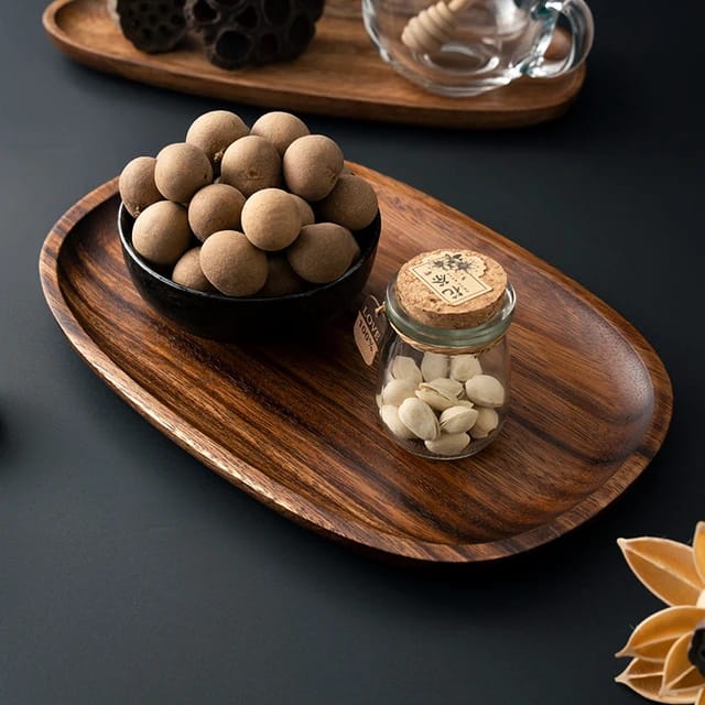 Irregular oval wood serving platter holding bowl of wooden balls and glass jar