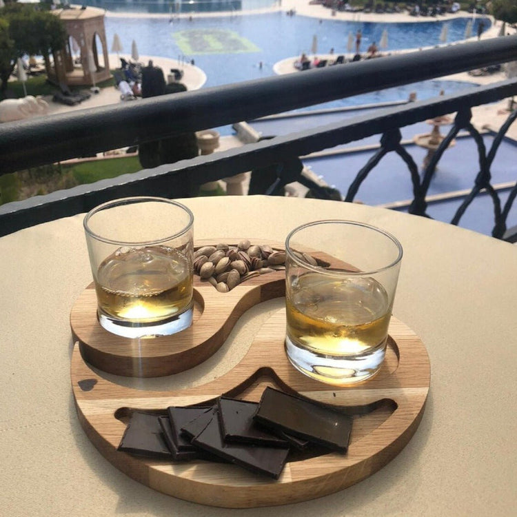 Yin yang wood serving platter with two drinks and chocolate on balcony table