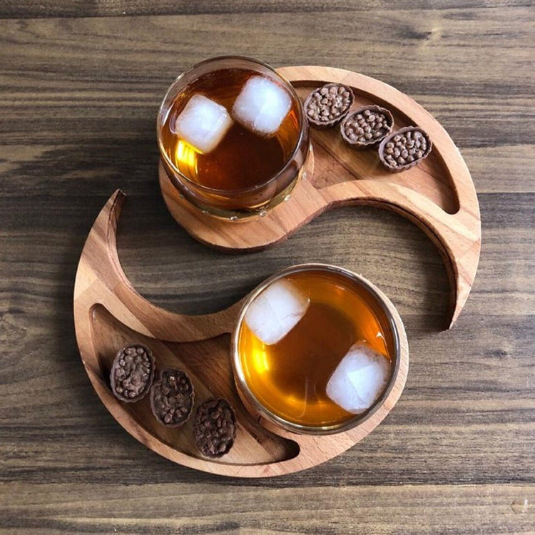 Yin yang wooden snack platter with whisky glasses and chocolates on table